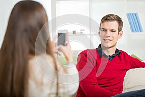 Girl photographs her boyfriend in the living room.