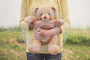 The girl picked up the brown teddy bear for carrying around and stood in the park to prepare for the special person