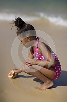 Girl picking up conch shell.