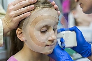 Girl pierced ear in the beauty salon. Adorable little girl having ear piercing process with special equipment in beauty center by