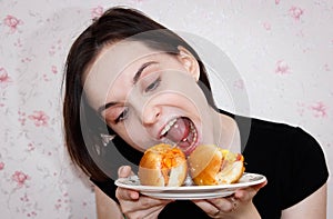A girl with a piercing in her tongue and a grimace on her face tries to bite off a hot dog on a plate