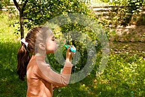 a girl with a pigtail blows soap bubbles on a sunny summer day