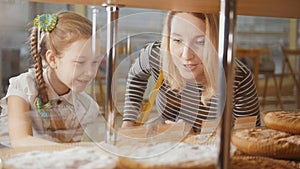 Girl with a pigtail and her mom look at the pies in the window choosing