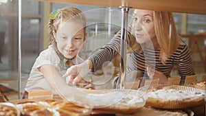 Girl with a pigtail and her mommy look at the pies in the window choosing