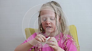 a girl with pigtails blows her nose, a 7-year-old girl is sick and empties her nose with a napkin