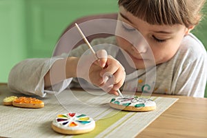 Girl with pigtails paints Easter glazed cookies with a brush while sitting in the kitchen at the table