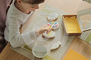 Girl with pigtails paints Easter glazed cookies with a brush while sitting in the kitchen at the table