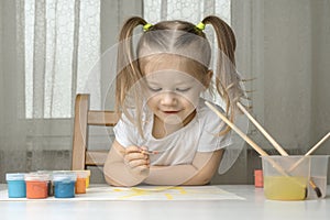 Girl with pigtails sits on a chair and paints the sun with a brush with yellow paint