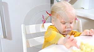 A girl with pigtails sits at the table and pushes a plate of food away from her, refuses to eat.