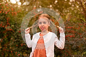 Girl with pigtails sits on a textured stone among autumn foliageportrait of a little cute girl with pigtails among the