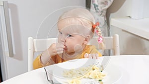 A girl with pigtails is sitting at the table and eating Farfalle pasta with a fork.