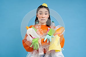 Girl with piles of garbage, surrounded by litter, looks concerned, sorts waste and recycles, blue background