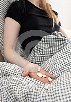 Girl with pills in hand with selective focus at bed. Woman feeling sick at home, indoors. Concept flu, headaches