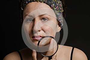 Girl with a pimply face holding magnifying glass. Woman skin care concept caucasian girl on black background photo