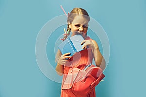 Girl with pink bag bites notebook. Kid with naughty face