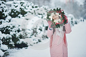 Girl in pink coat in snow Park. Girl plays in winter Park. Adorable child walking in snow winter forest touch wood branch on tree.