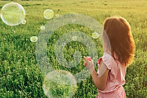 Girl in pink dress blowing soap bubbles in summer