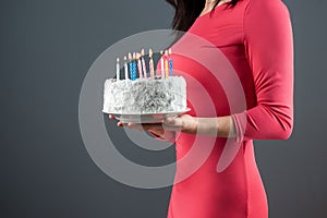 A girl in a pink dress holds in her hands a cake with burning candles, close-up. Happy birthday congratulation celebration party