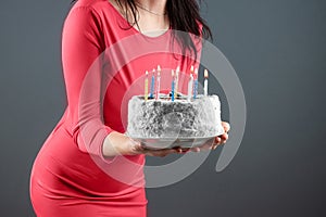 A girl in a pink dress holds in her hands a cake with burning candles, close-up. Happy birthday congratulation celebration party