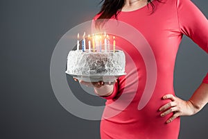 A girl in a pink dress holds in her hands a cake with burning candles, close-up. Happy birthday congratulation celebration party