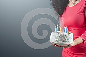 A girl in a pink dress holds in her hands a cake with burning candles, close-up. Happy birthday congratulation celebration party