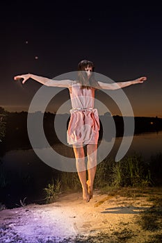 Girl in pink dress jumping on the river beach during sunset and white flour on the ground photo