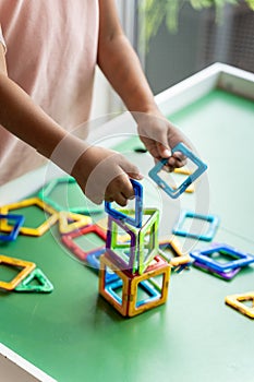 Girl in pink dress playing with magnetic geometric shape toy, hands show, no face.