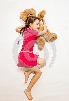 Girl in pink dress sleeping on big teddy bear on floor