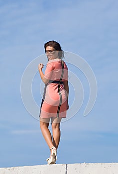 Girl in pink dress walking against the sky