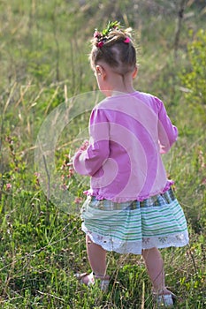 Girl in a pink dress walking on meadow of grass and flowers