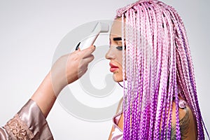 A girl with pink hair braids with non-contact thermometer on white background