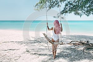 Girl with pink hair hanging on swing at beach