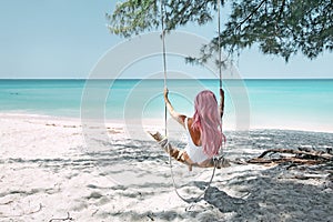 Girl with pink hair hanging on swing at beach