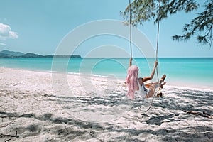 Girl with pink hair hanging on swing at beach