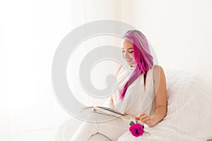 The girl with the pink hair is reading a book in a white room