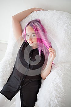 Girl with pink hair sits in a Chair in a white room