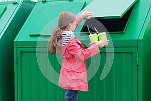 A girl in a pink jacket carries disposable glasses with tubes in a dumpster to throw them away