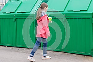 A girl in a pink jacket, carrying disposable glasses in a dumpster to throw them away