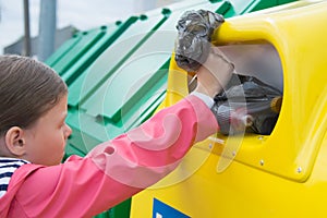 Girl in a pink jacket, throws a bag of garbage into a container, close-up