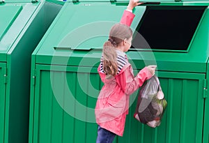 A girl in a pink raincoat brought a bag of garbage and throws it open the container