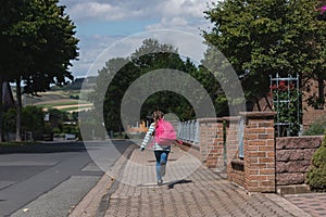 A girl with a pink satchel on her back runs down the street to school. The first day of school, the children are ready to study