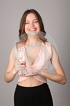 Girl in pink shirt holding bottle of water. Close up. Gray background