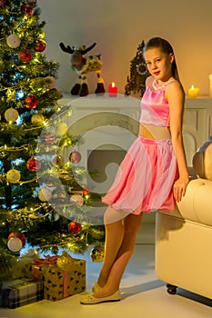 Girl in a pink skirt and T-shirt posing near the Christmas tree.