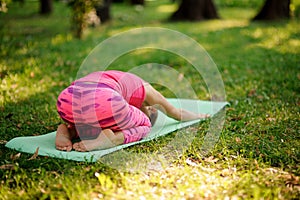 Girl in the pink sportsuit practice yoga in the park in Child`s Pose