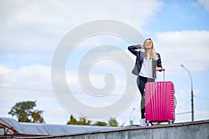 Girl with a pink suitcase on a background of a beautiful blue sky