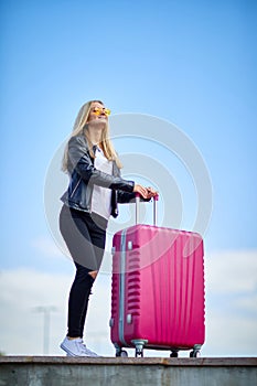 Girl with a pink suitcase on a background of a beautiful blue sky