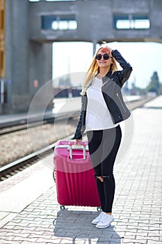 A girl with a pink suitcase is standing at the railway station