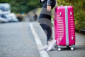 A girl with a pink suitcase stands on the street close up