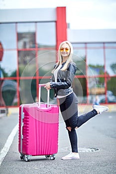 A girl with a pink suitcase stands on the street close up