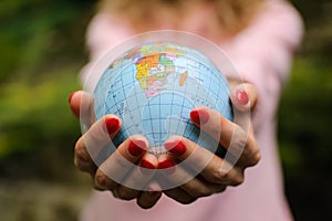 The girl in a pink sweater with red manicure holds a small globe with geografical names in Ukrainian cyrillic letters on